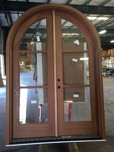 an arched wooden door with glass on the outside and inside, sitting in a warehouse