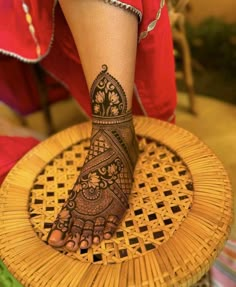 a woman's foot with henna tattoo on it sitting on a wicker chair