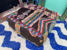 a multicolored ottoman sitting on top of a blue rug next to a mirror