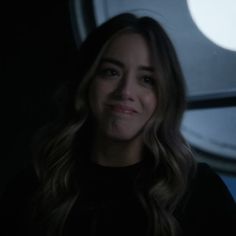 a woman with long hair standing in front of an airplane window at night, smiling