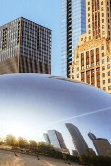 a large metal ball in the middle of a city with tall buildings behind it and people walking around