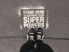 a person standing on the sidewalk with their feet up in front of a sign that says, stand here to activate your super powers