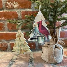 two small christmas trees sitting next to each other on a stone floor near a brick wall