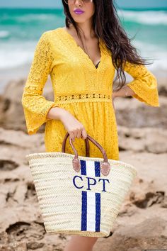 a woman in yellow dress holding a white and blue striped straw bag on the beach