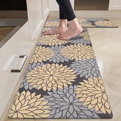 a person standing on top of a kitchen floor next to a rug with yellow and gray flowers