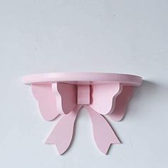 a pink shelf with two bow shaped shelves on the top and bottom, against a white wall