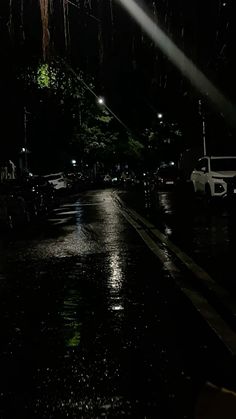 a street at night with cars parked on the side of the road and one person holding an umbrella