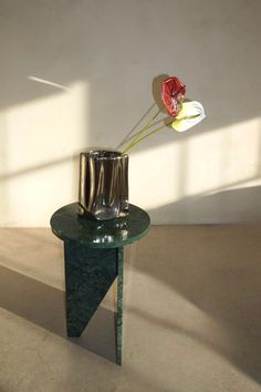 a vase with two flowers in it sitting on a small table next to a wall