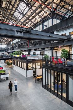 two people walking through an open building with lots of windows and plants on the roof