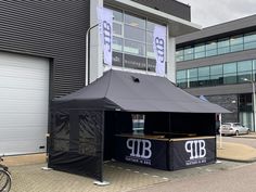 a large black tent sitting on the side of a road next to a tall building