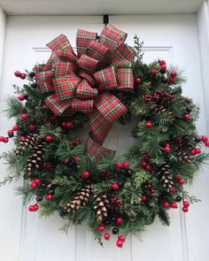 a christmas wreath with pine cones and red berries hanging on the front door for decoration