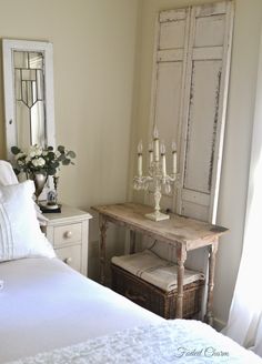 a white bed sitting next to a wooden dresser and table with candles on top of it