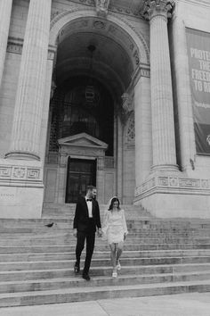 a man and woman walking up some steps in front of a large building with columns