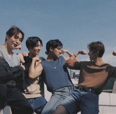 four young men are posing for the camera on top of a building with their arms in the air