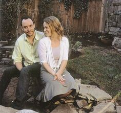 a man and woman sitting next to each other on a stone slab in front of a fence