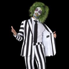 a man dressed up as a clown with green hair and makeup holding a suit on his chest