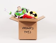 a cardboard box filled with toy cars on top of a white table next to a sign that says noah's toys