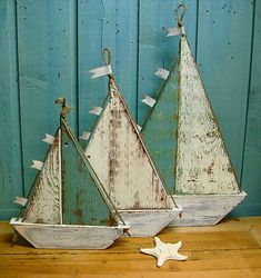 three wooden sailboats are sitting on a table next to each other and one has a star hanging from it