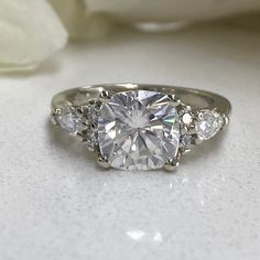 three stone diamond ring on white surface with flowers in the backgroufground