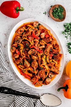 a white bowl filled with pasta and meat on top of a table next to tomatoes