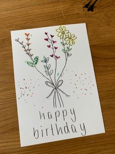 a happy birthday card with flowers and butterflies on the front, sitting on a wooden table