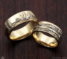 two gold wedding rings sitting on top of a wooden table