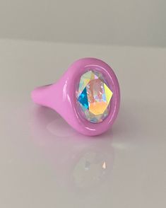 a pink ring with an iridescent colored diamond in the center on a white surface