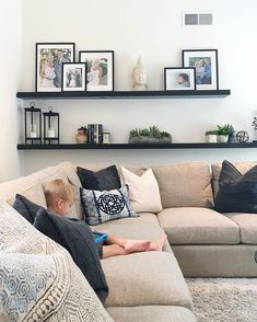 a young boy sitting on top of a couch in front of a wall filled with pictures