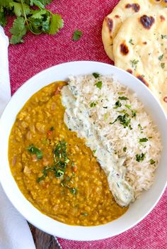 a white bowl filled with rice and curry next to some pita bread on a red table cloth