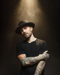 a man with tattoos and a hat on posing for a photo in front of a spotlight