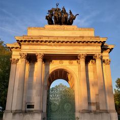 an arch with statues on the top and sides in front of blue sky at sunset