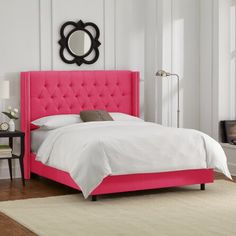 a pink bed with white sheets, pillows and a mirror on the wall above it