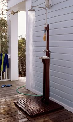 an outdoor shower on a wooden deck next to a white house with blue and green towels