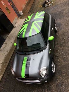 a small car with green and black stripes parked on the side of the road next to a building