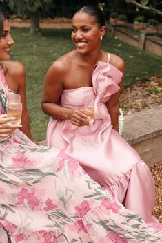 two women in pink dresses sitting next to each other and holding wine glasses with their hands