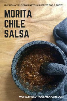 a bowl filled with chili sauce on top of a wooden table next to a blue towel