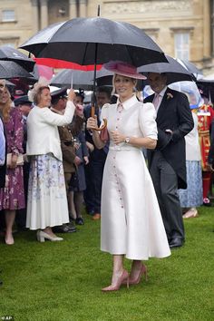 a woman in a white dress and hat holding an umbrella while standing next to other people