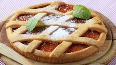 a fresh fruit pie with powdered sugar and mint leaves on top, sitting on a wooden platter