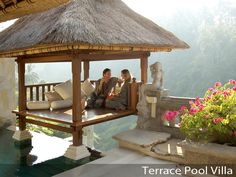 two people sitting on a bench in front of a gazebo with flowers and greenery