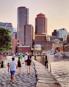 people walking along the water in front of some tall buildings and other large city buildings