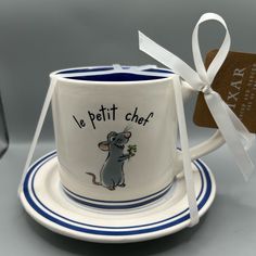 a white and blue coffee cup with a mouse painted on it, next to a tag that says le petit chef