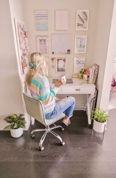 a woman sitting at a desk with a cup in her hand and pictures on the wall behind her