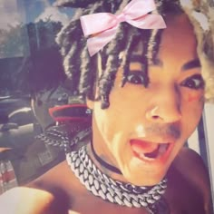 a woman with dreadlocks and a pink bow on her head is making a funny face