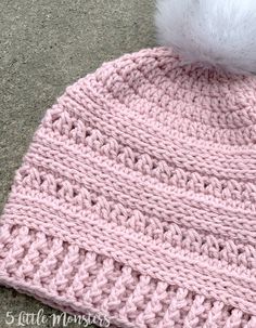 a crocheted hat with a white pom - pom on top is laying on the ground