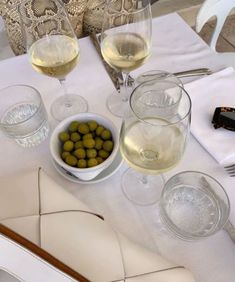 two glasses of white wine and some olives on a table with other food items