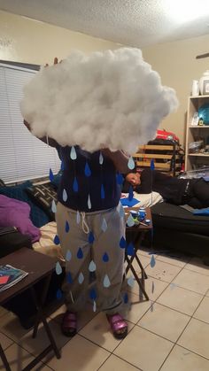 a person standing in a living room with a cloud on top of their head and rain drops falling from the clouds