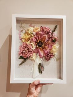 a person holding up a white frame with flowers in it