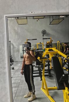 a shirtless man taking a selfie in front of a gym machine with his cell phone