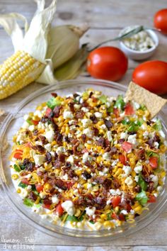 a glass bowl filled with corn, tomatoes, and other food items next to some corn on the cob