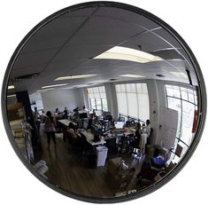 an office with people working on computers in the reflection of a round mirror that is hanging from the ceiling